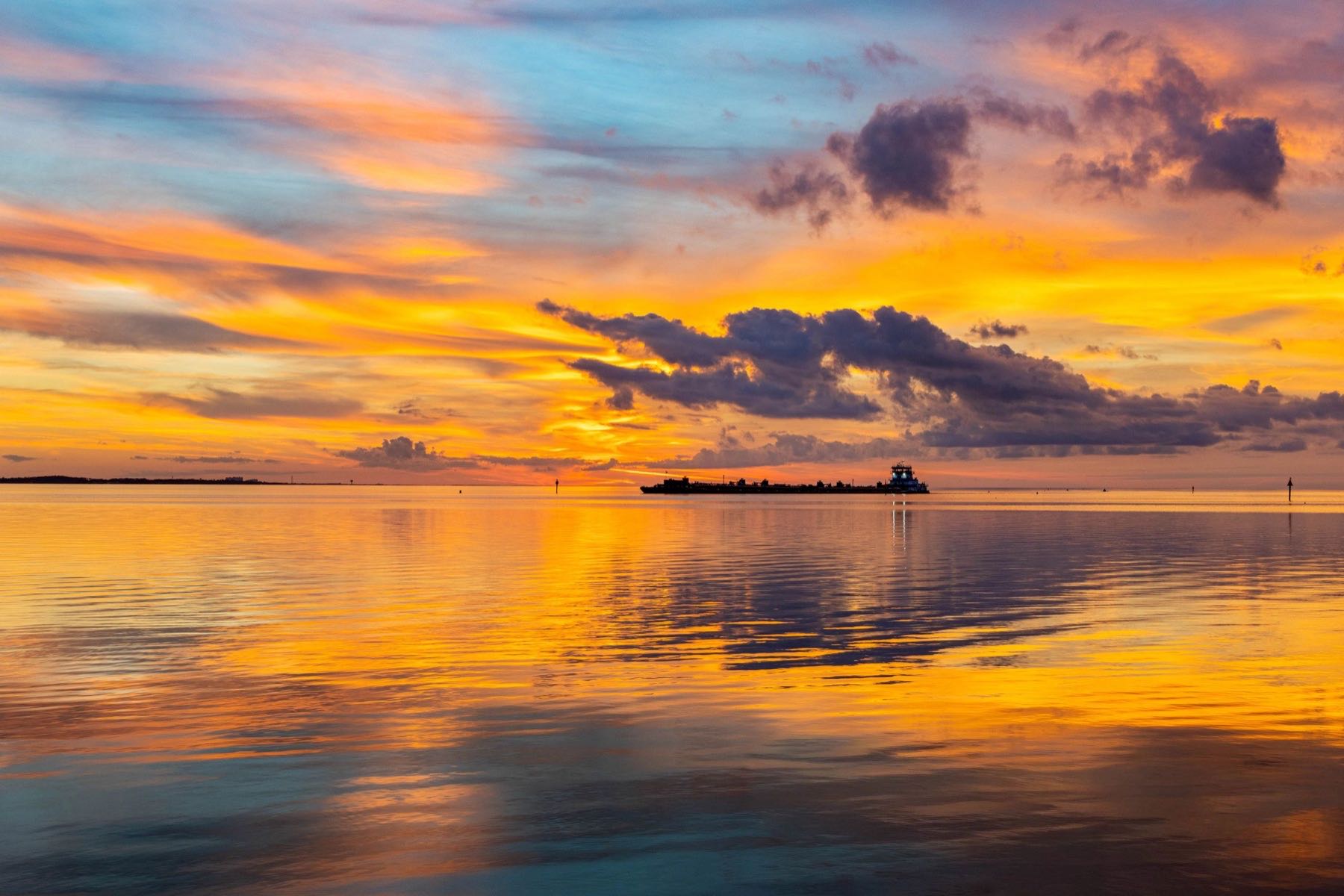 Tugboat and barge silhouetted against a vivid Gulf Coast sunset