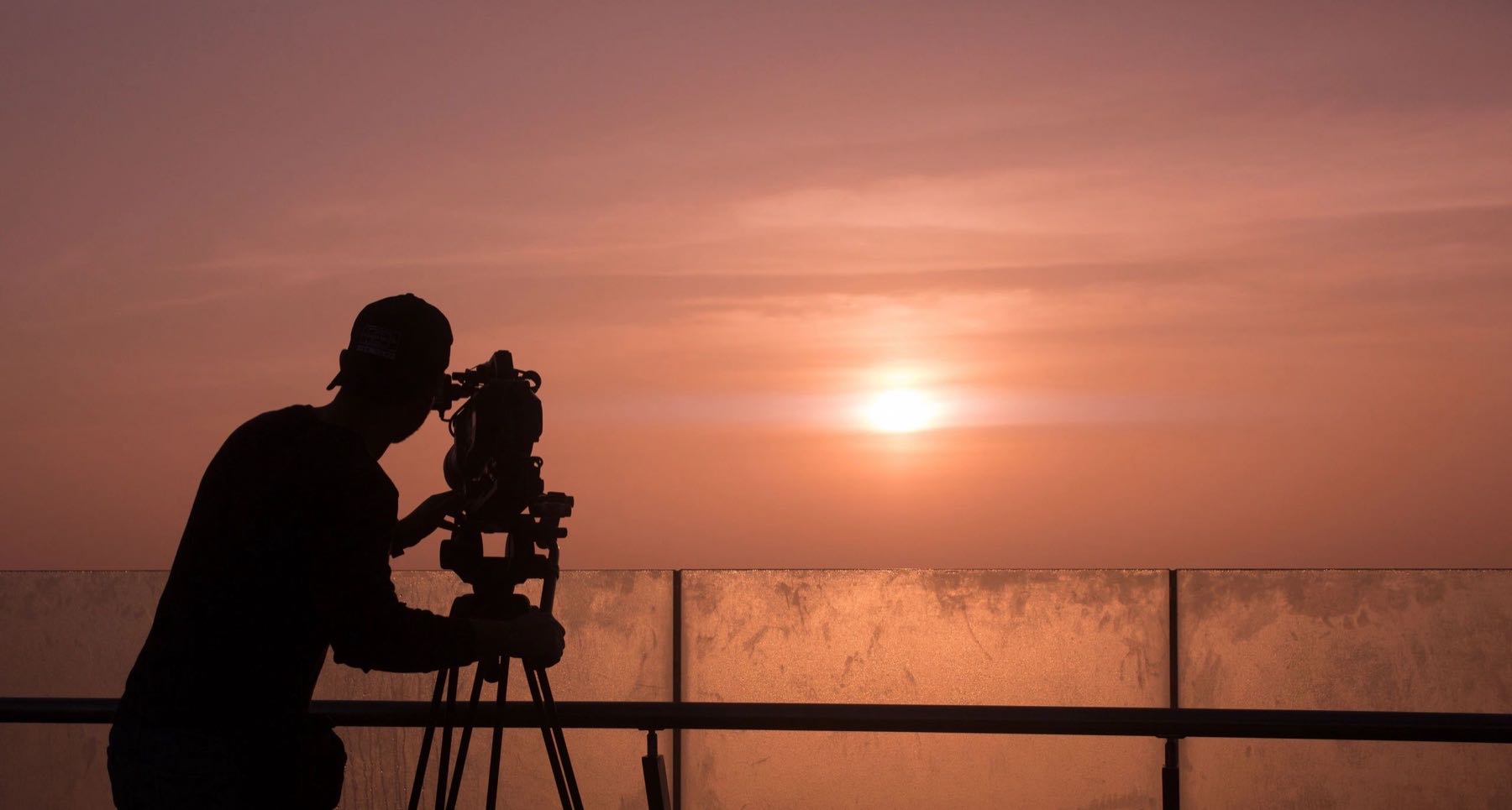 Silhouette of a camera operator on a tripod filming at sunset