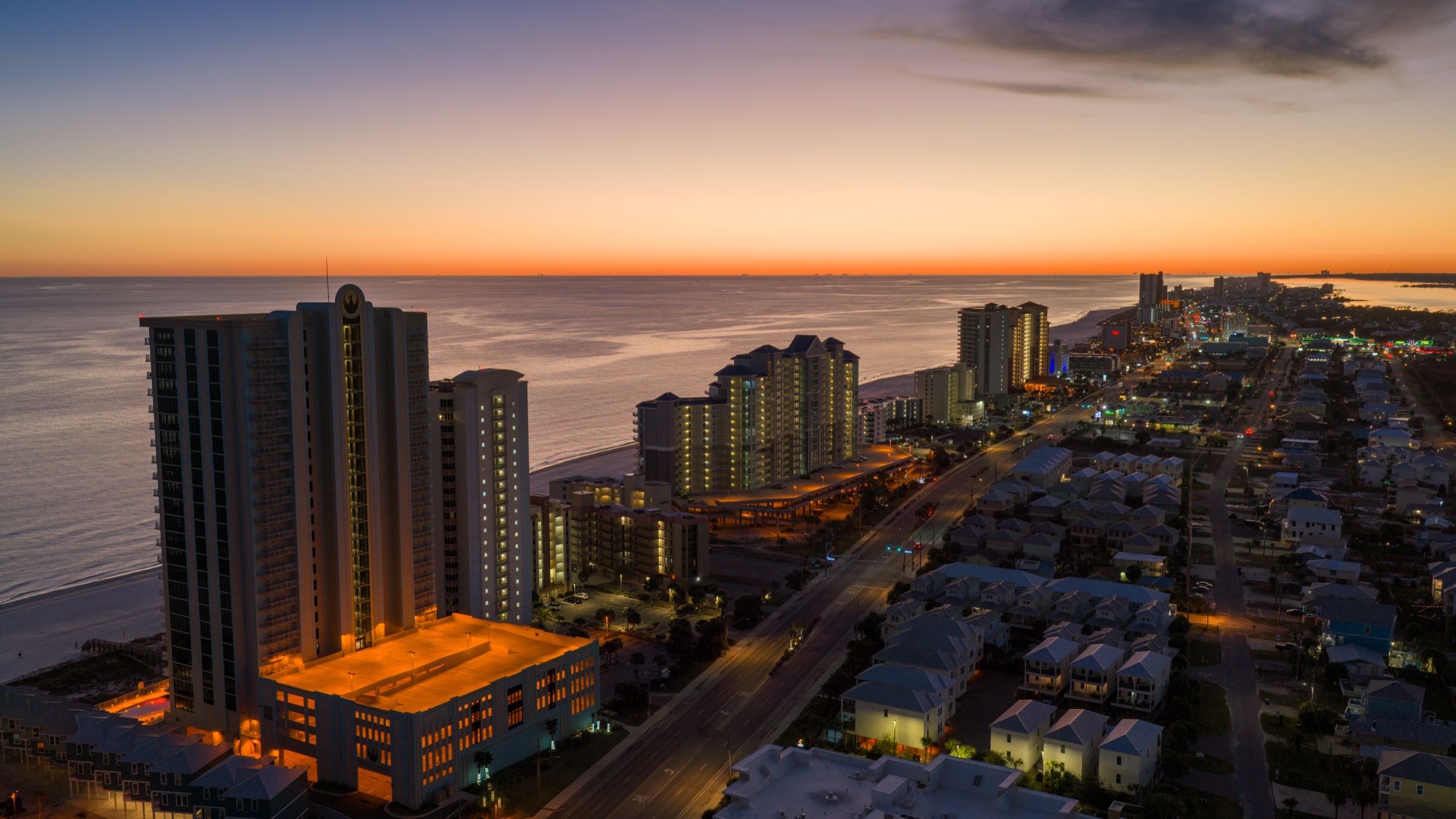 Gulf Shores skyline lit up at dusk with the sun setting over the water