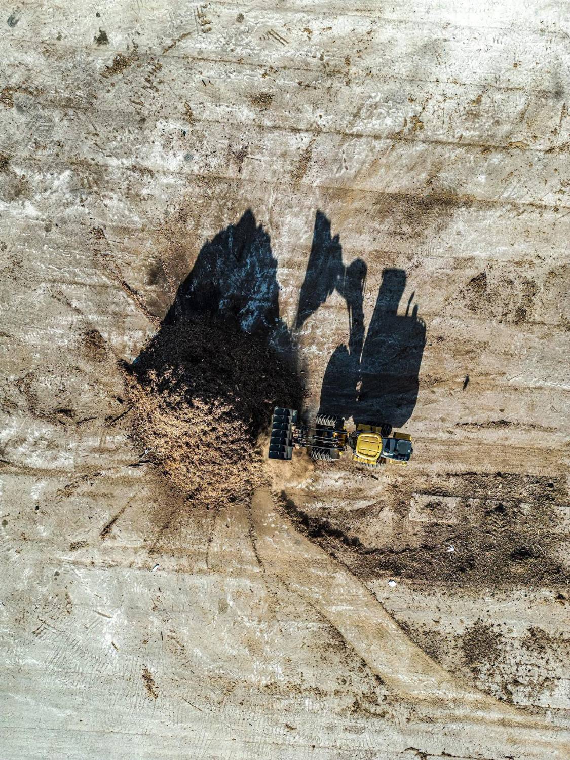 Aerial view of an excavator and its long shadow working a construction site