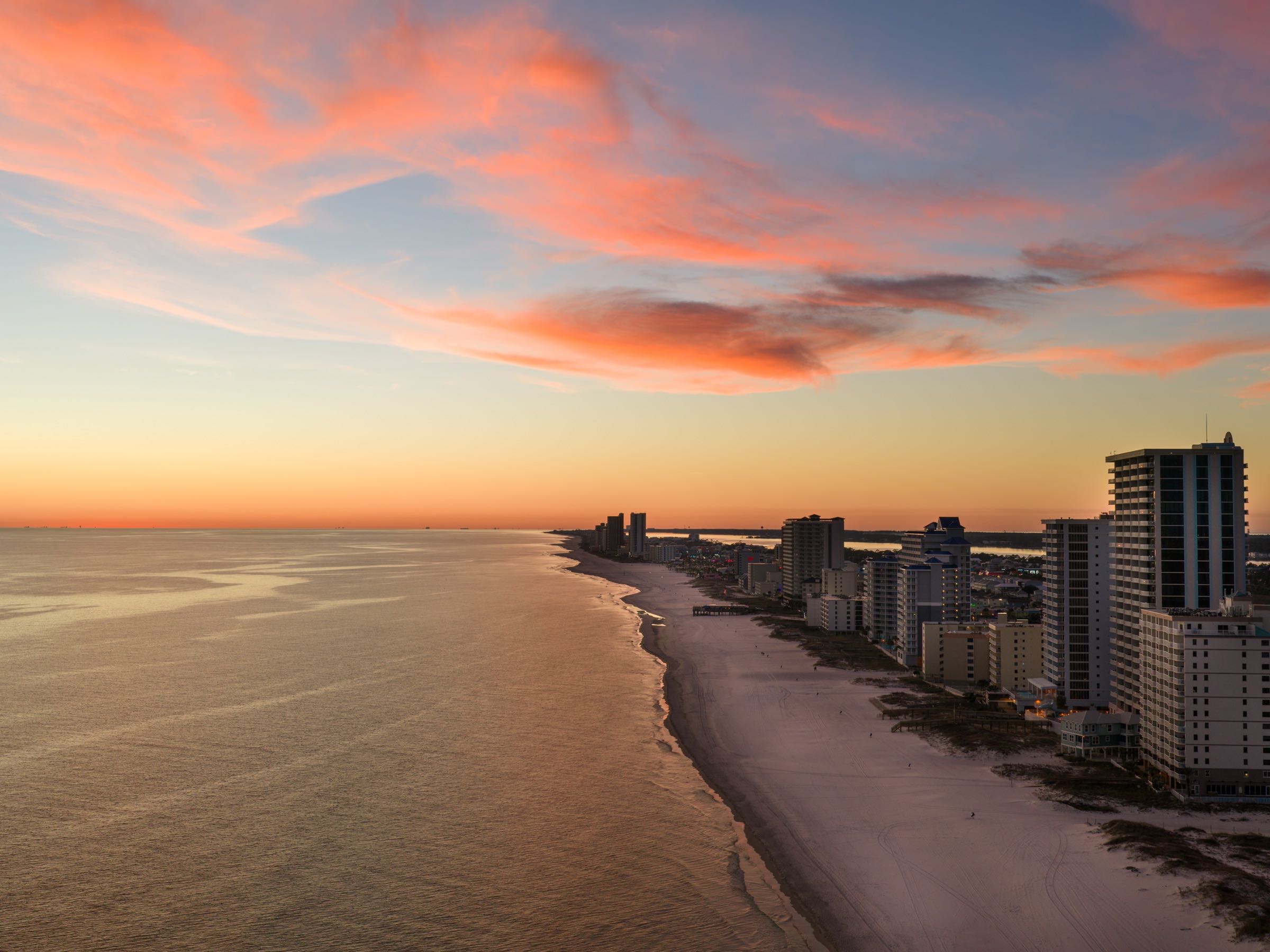 Aerial view of the Alabama Gulf Coast at sunset, condo towers along a lit shoreline