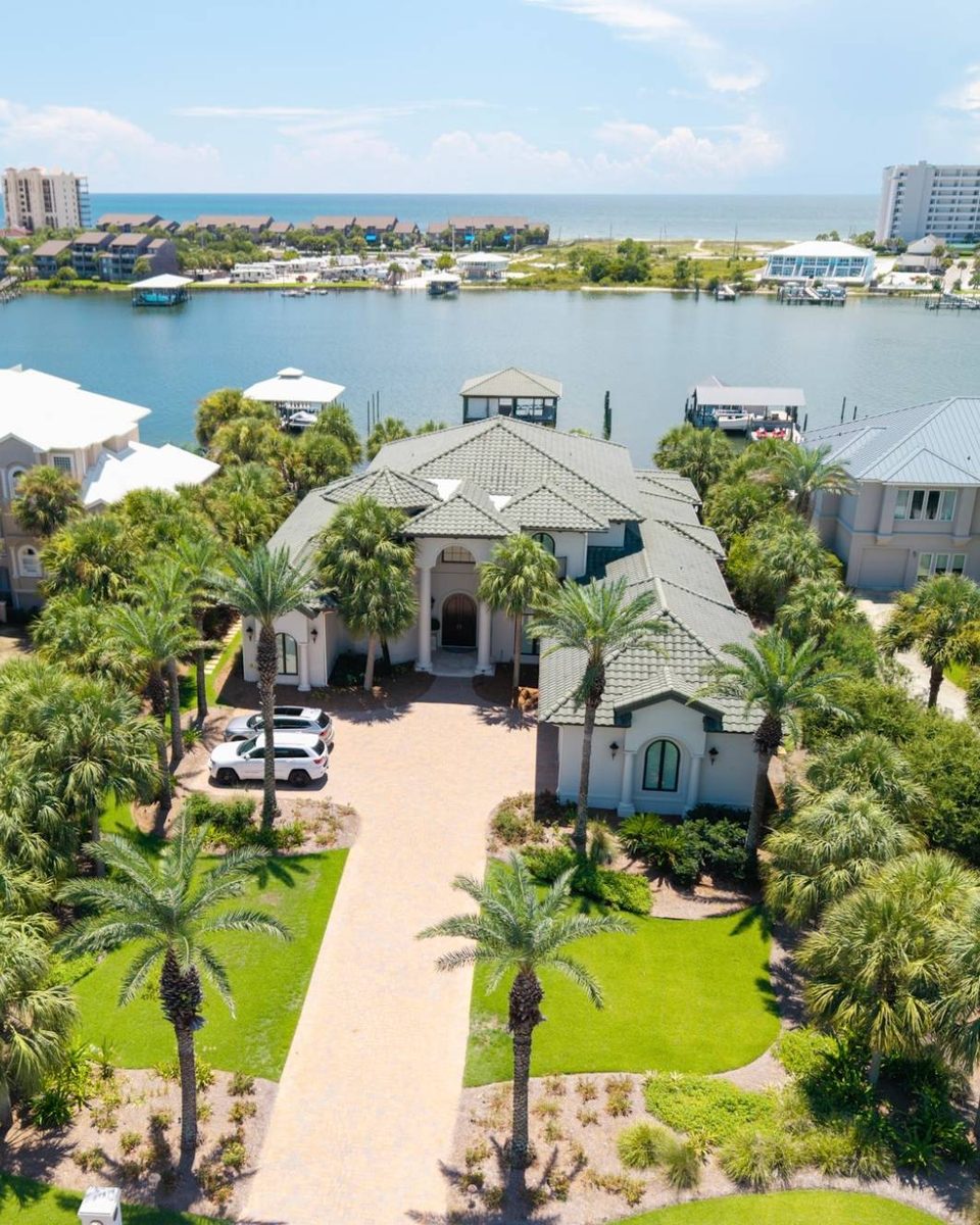 Aerial view of a Mediterranean-style waterfront estate with a paver driveway and palms