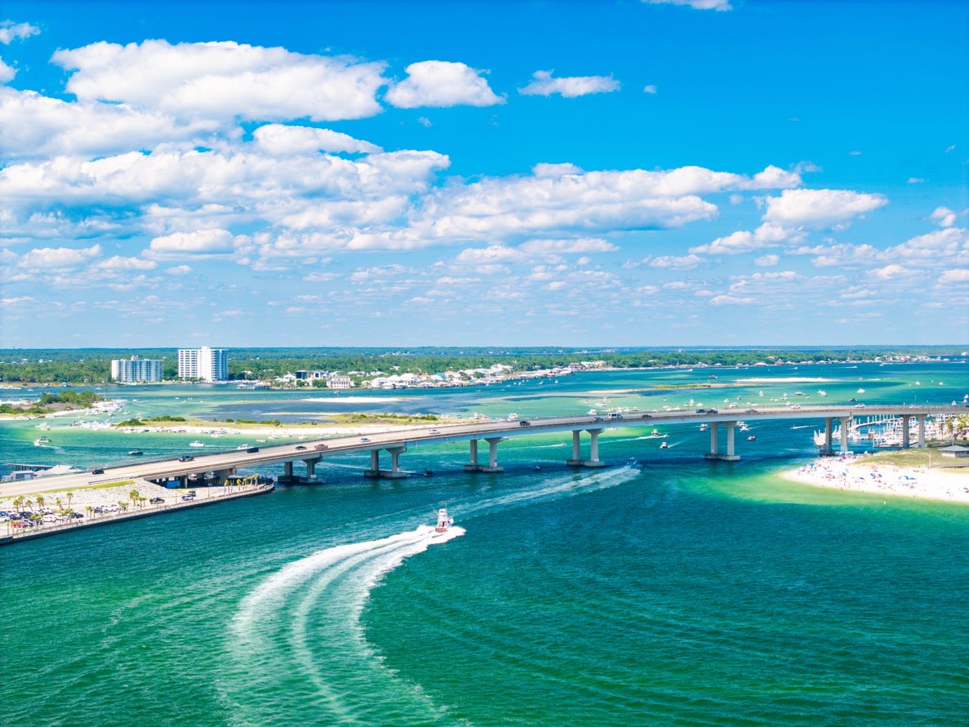 Aerial view of a bridge over a turquoise inlet with a boat wake